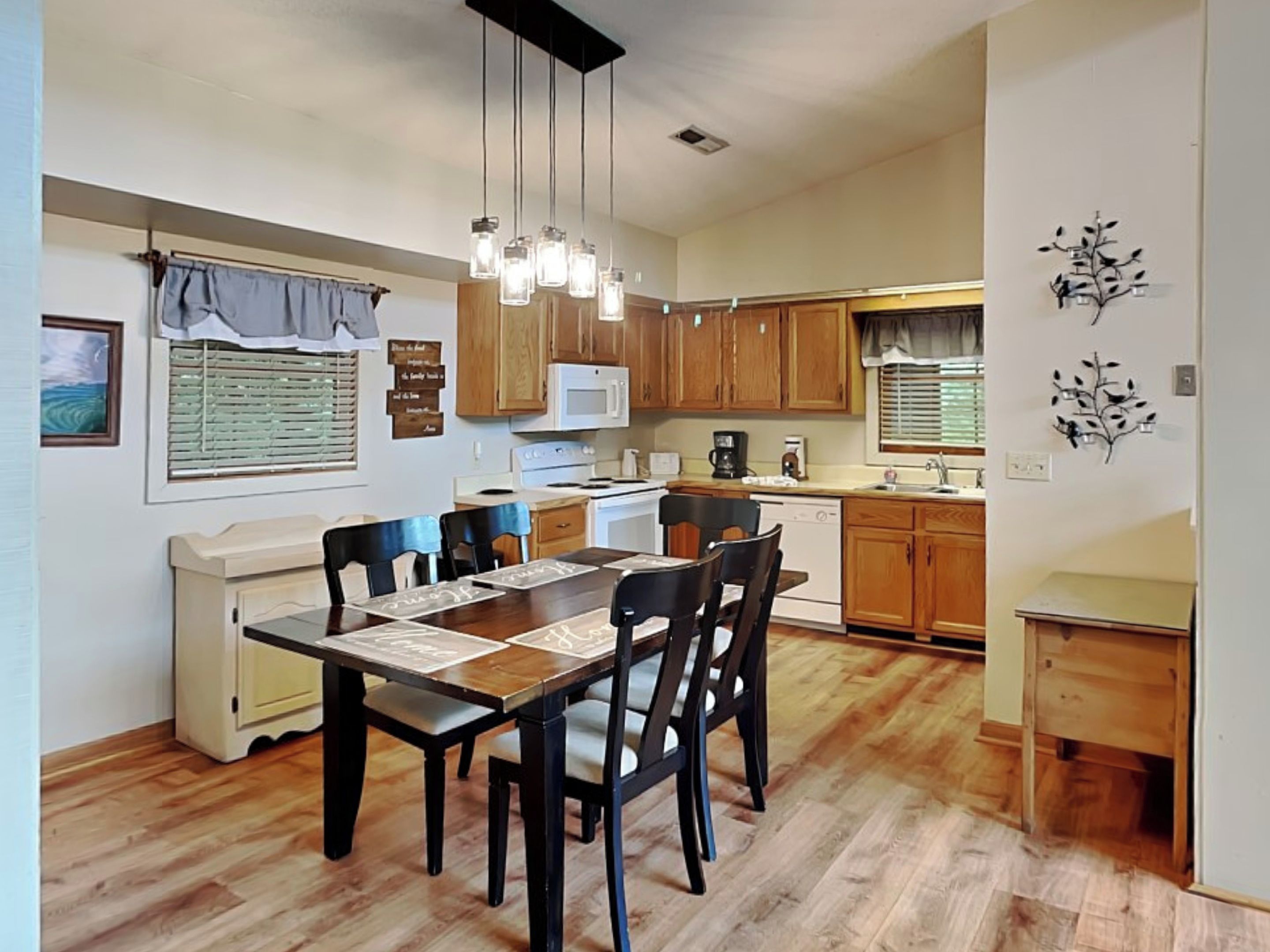 A modern kitchen with wooden cabinets, a dining table with chairs, and pendant lighting.