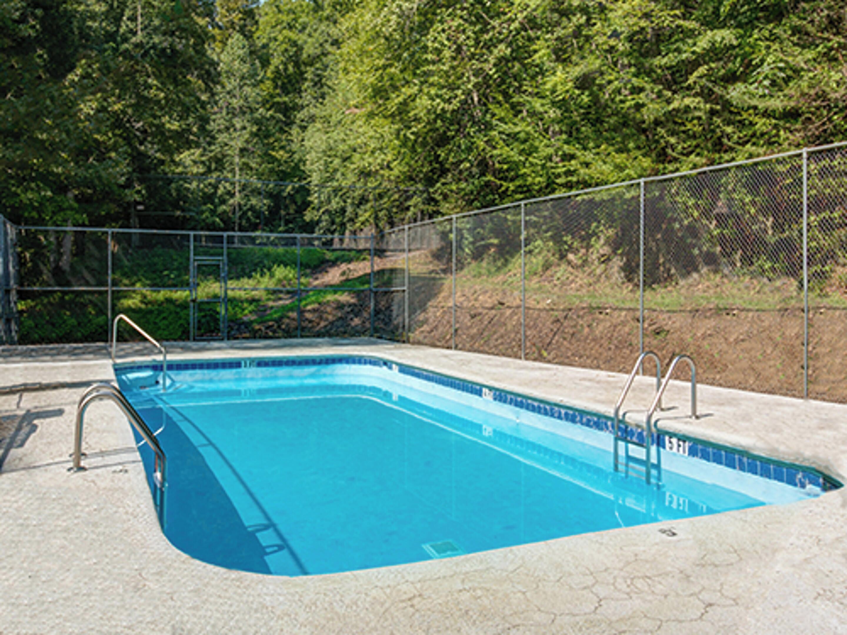 A rectangular swimming pool with a blue interior, surrounded by a metal fence and concrete deck.