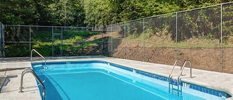 Una piscina rectangular con revestimiento azul, rodeada por una valla metálica y un suelo de hormigón.