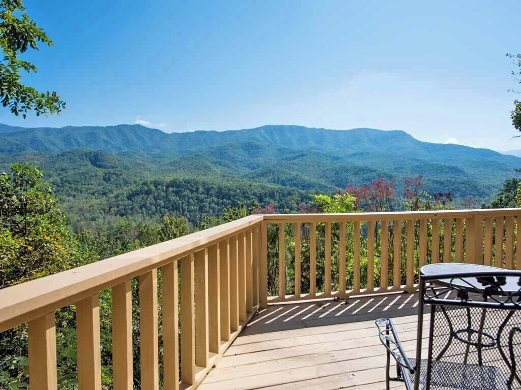 Una terraza de madera con una mesa y sillas, con vistas a un paisaje montañoso.
