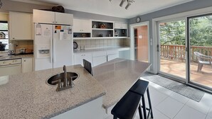 A modern kitchen with a large island, white cabinetry, and a sliding glass door leading to an outdoor deck. - Shooting Star by Jackson Mountain Rentals (Gatlinburg)