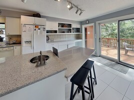 Una cocina moderna con una isla grande, armarios blancos y una puerta corrediza de vidrio que da a una terraza al aire libre.