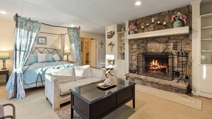 A bedroom with a four-poster bed, a glass coffee table, a fireplace, and a stone wall. - Shooting Star by Jackson Mountain Rentals (Gatlinburg)