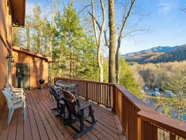 A wooden deck with outdoor furniture, a grill, and a view of a forest and mountains.