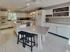 A modern kitchen with white cabinets, a granite countertop, and a central island with stools. - Shooting Star by Jackson Mountain Rentals (Gatlinburg)