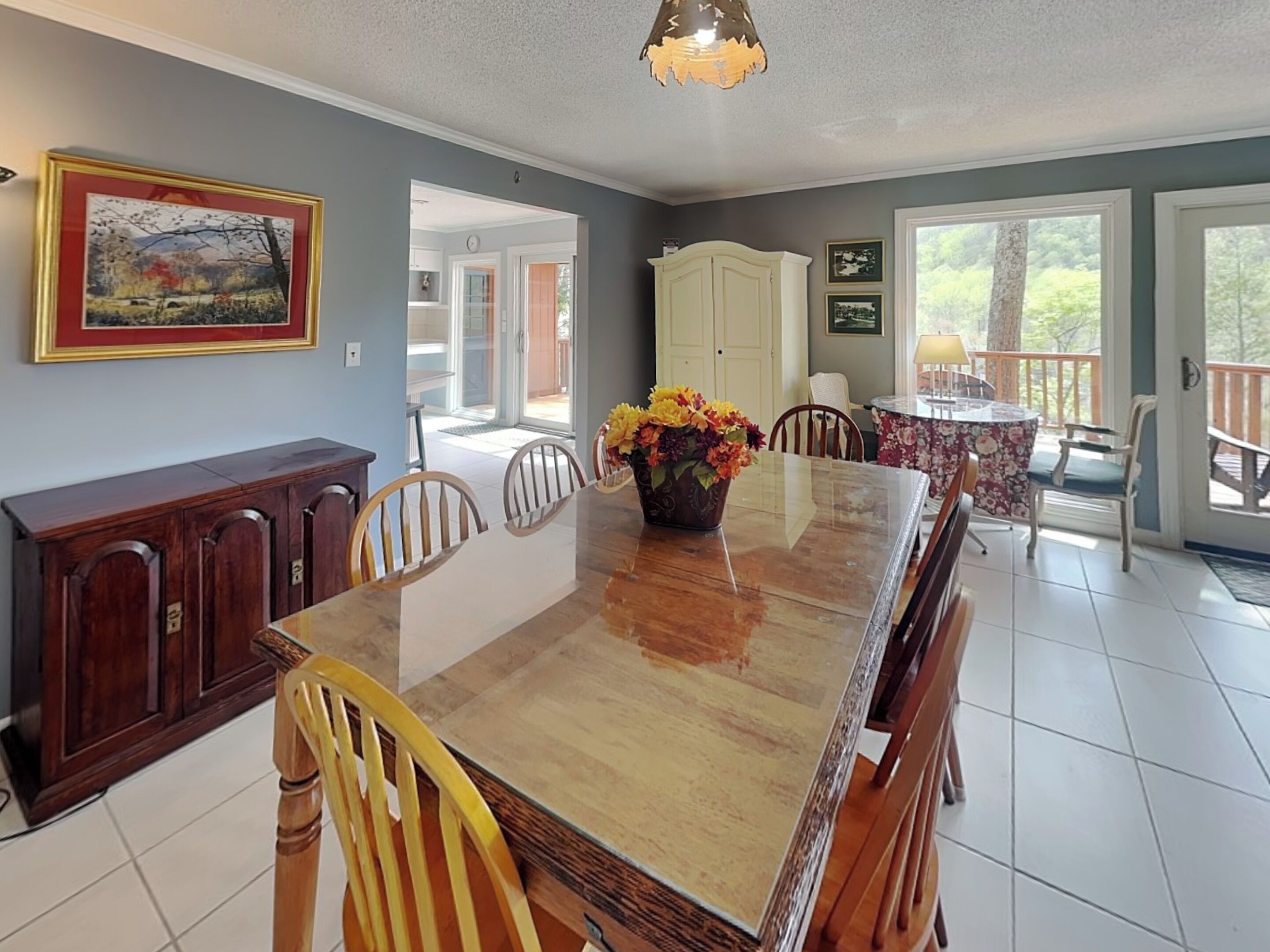 Uma sala de jantar com mesa de madeira, cadeiras, um vaso de flores, um armário e um quadro na parede.