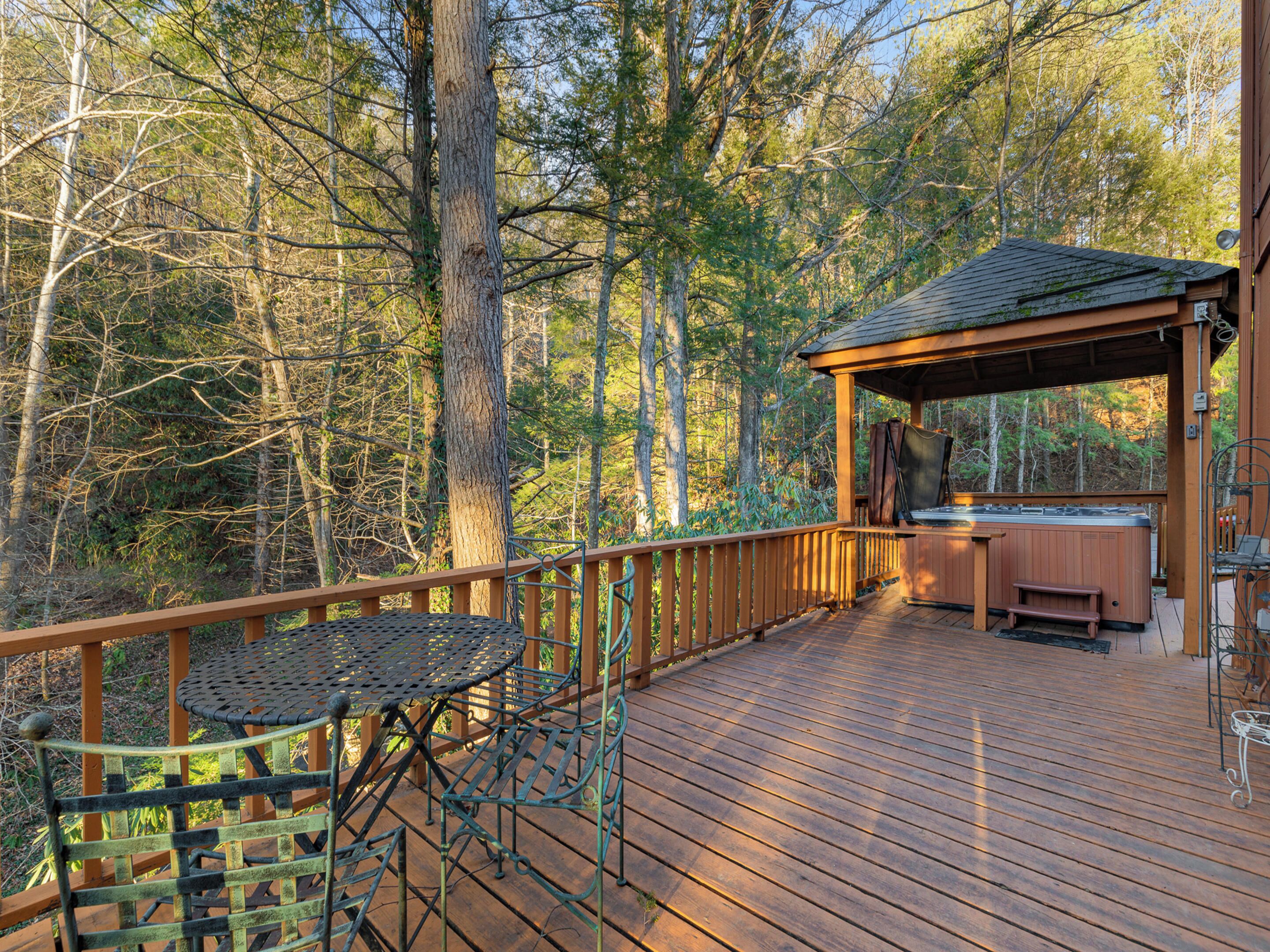A wooden deck with a hot tub and a covered seating area surrounded by trees.