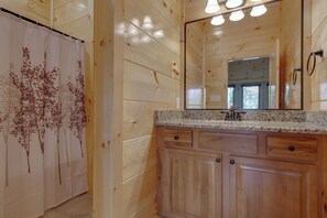 A wooden cabin bathroom with a shower curtain, a sink with a granite countertop, and a large mirror. - Smoky Mountain Splash by Jackson Mountain Rentals (Gatlinburg)