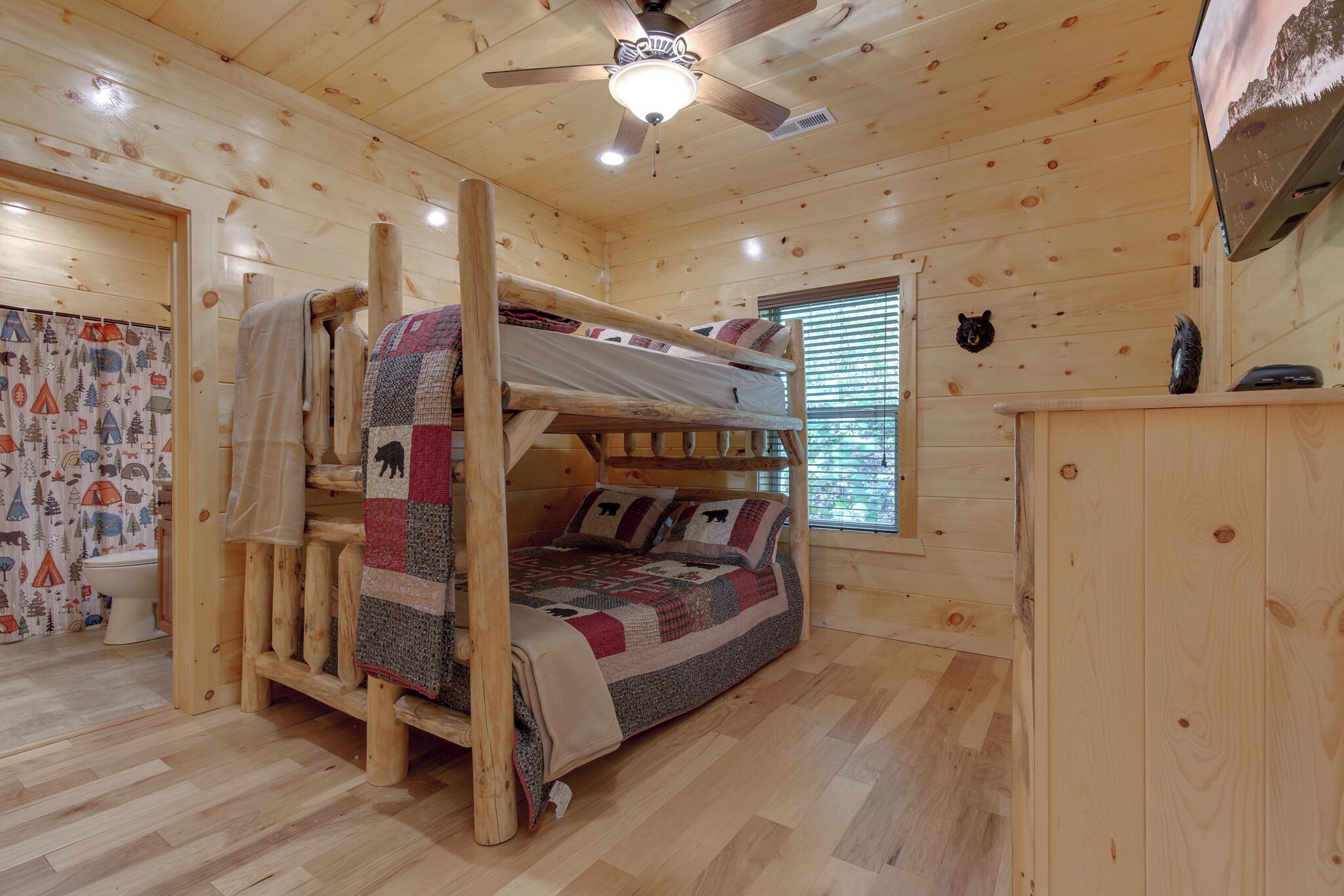 A wooden cabin room with a bunk bed, a ceiling fan, a TV, and a bear decoration.