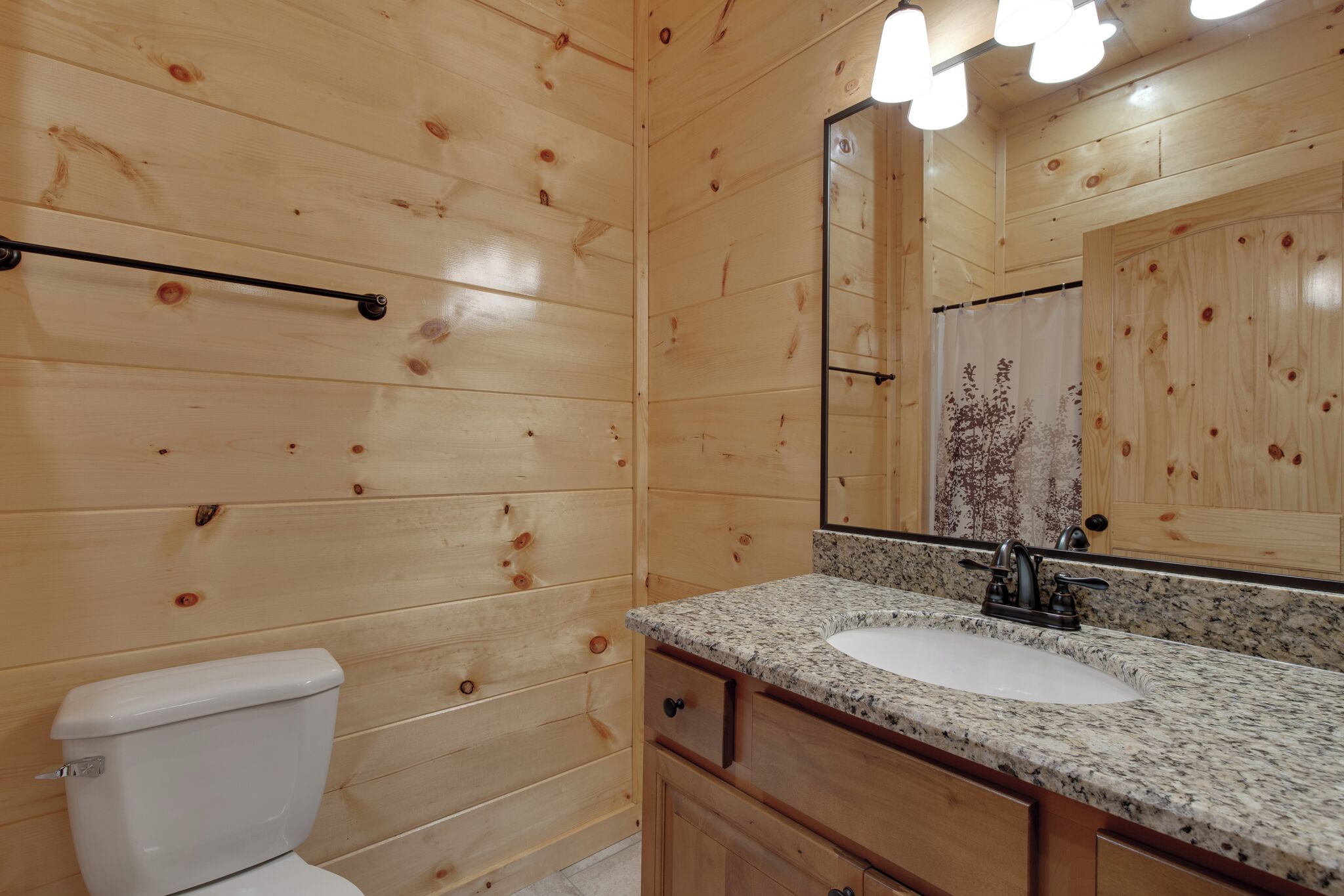 Un baño con paneles de madera, inodoro blanco, lavamanos de granito y un espejo grande.