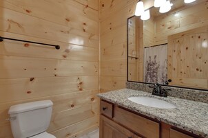Ein Badezimmer mit Holzwandverkleidung, einer weißen Toilette, einem Waschbecken mit Granitplatte und einem großen Spiegel.