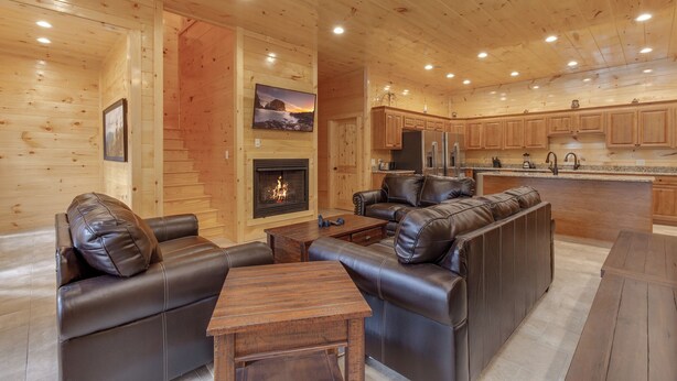 L’intérieur d’un chalet confortable, avec une cheminée, des canapés en cuir, des meubles en bois et un coin cuisine.