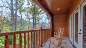 Un balcon en bois avec une balustrade, un fauteuil à bascule et une vue sur les arbres et les montagnes.