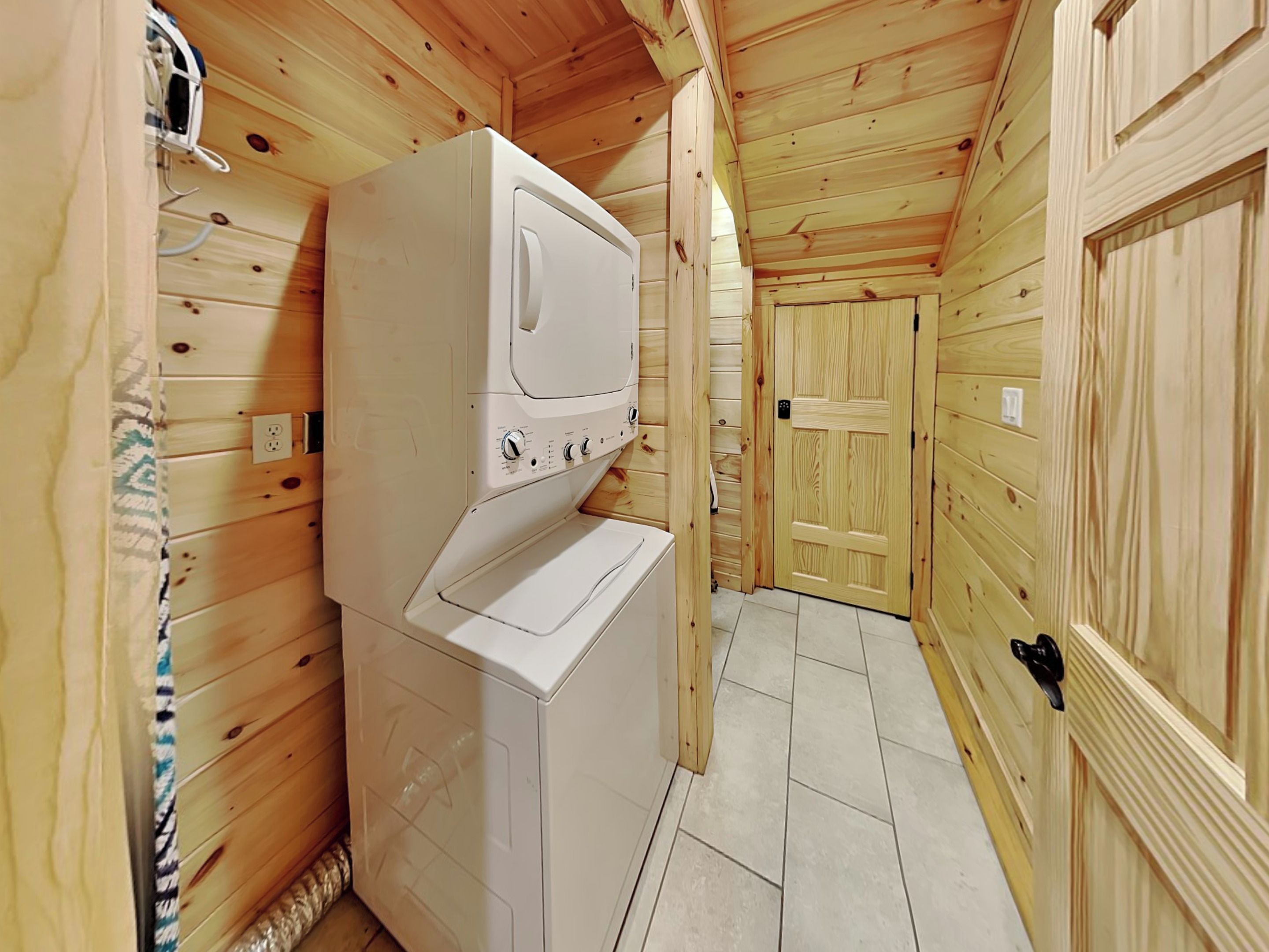 A compact, wooden interior with a white washer and dryer unit, a door, and a tiled floor.