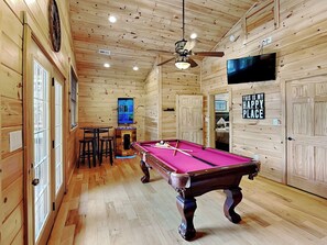 Un intérieur en bois avec une table de billard, un ventilateur de plafond et un téléviseur fixé au mur.