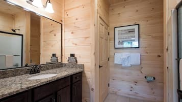 A wooden cabin bathroom with a granite countertop sink, dark wooden cabinets, a large mirror, and a framed picture on the wall.