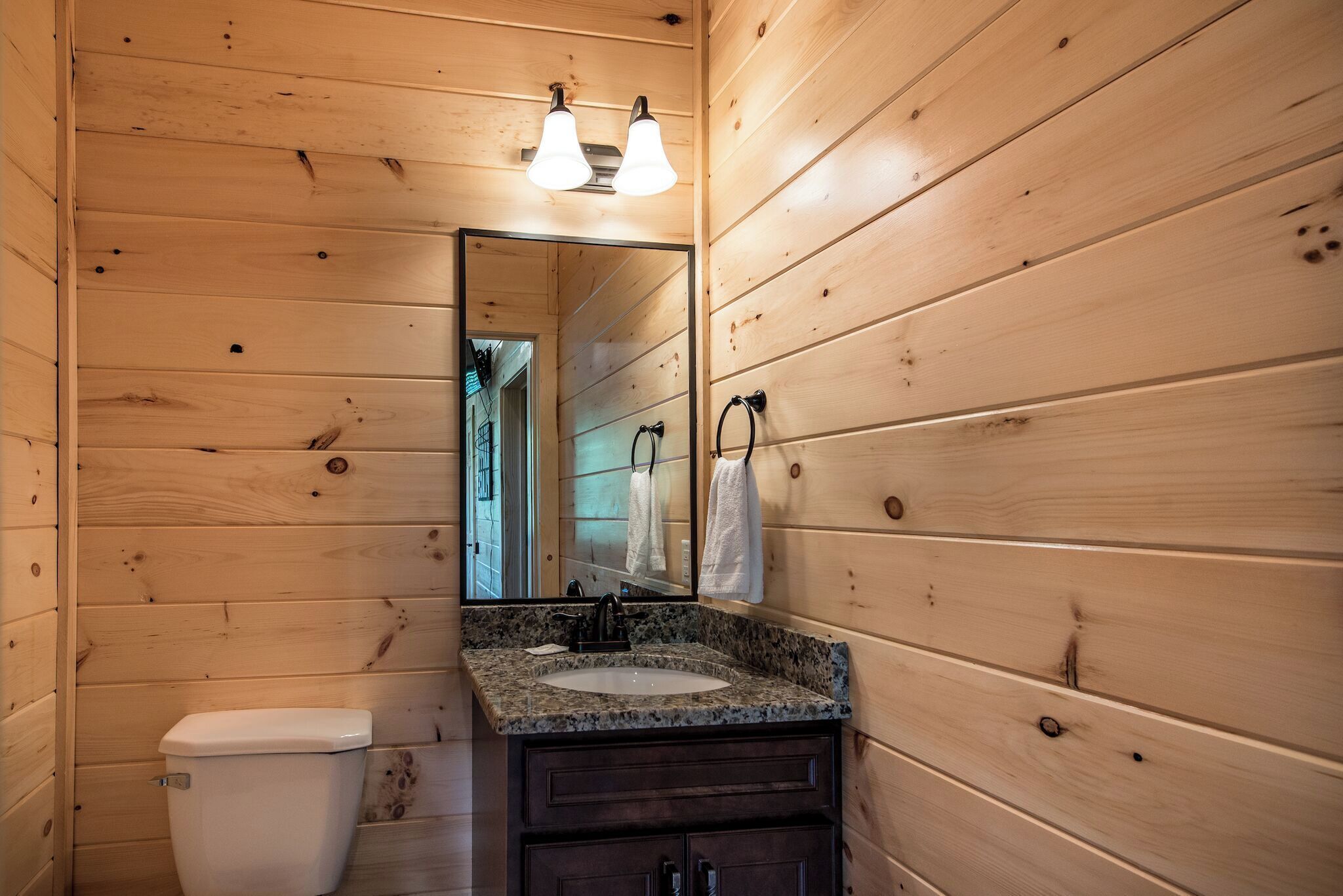 A wooden cabin bathroom with a sink, mirror, and toilet.