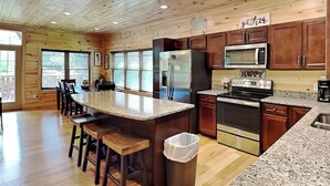 A spacious kitchen with wooden cabinets, a granite countertop, stainless steel appliances, and a bar area with stools. - Smoky Haven by Jackson Mountain Rentals (Gatlinburg)