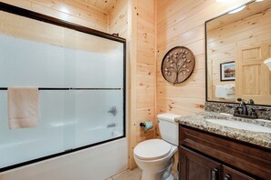 A bathroom with wooden walls, a glass shower door, a toilet, a sink with a granite countertop, and a mirror. - Smoky Haven by Jackson Mountain Rentals (Gatlinburg)