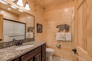 A wooden-paneled bathroom with a granite sink, a mirror, a toilet, and wooden wall decorations. - Smoky Haven by Jackson Mountain Rentals (Gatlinburg)