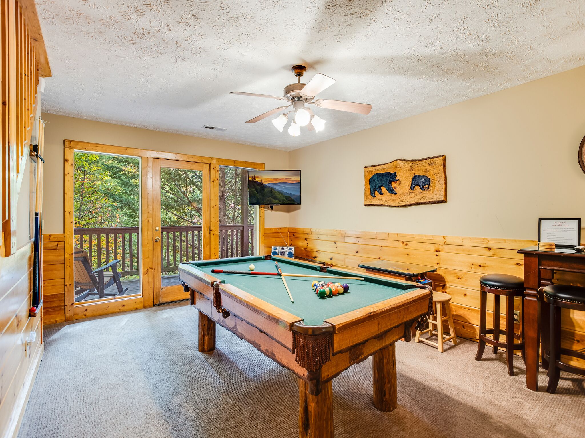 A pool table in a room with wooden walls and a ceiling fan.