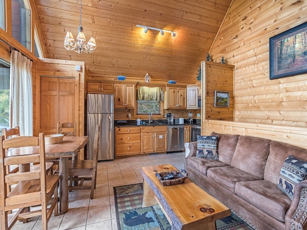 Ein gemütliches Blockhaus-Interieur mit Holzwänden, einem Essbereich mit Holztisch und -stühlen, einer Couch und einer Küche mit Holzausstattung und Geräten.