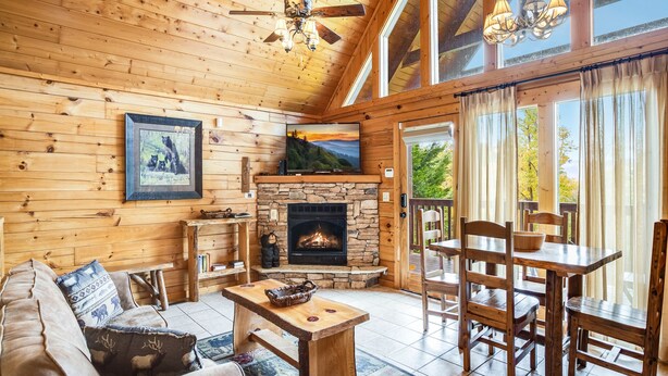 A cozy cabin interior with a stone fireplace, wooden furniture, and a television mounted above it. - Saddle Ridge by Jackson Mountain Rentals (Gatlinburg)