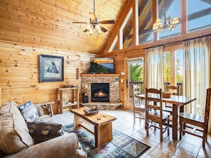 A cozy cabin interior with a stone fireplace, wooden furniture, and a television mounted above it.