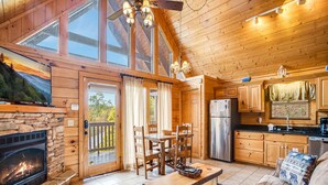 A cozy cabin interior with a stone fireplace, wooden dining table, and a sofa. - Saddle Ridge by Jackson Mountain Rentals (Gatlinburg)