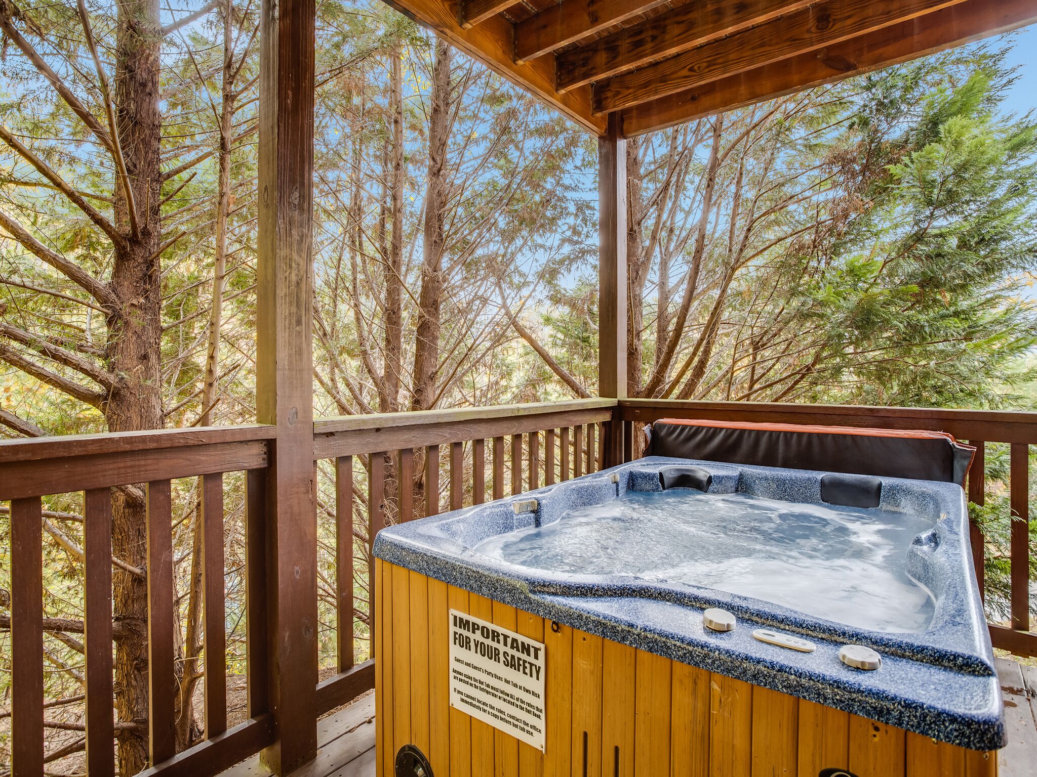 Una terraza de madera con un jacuzzi rodeado de árboles.