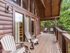 A wooden deck with Adirondack chairs, a covered area, and a view of the surrounding forest. - Saddle Ridge by Jackson Mountain Rentals (Gatlinburg)