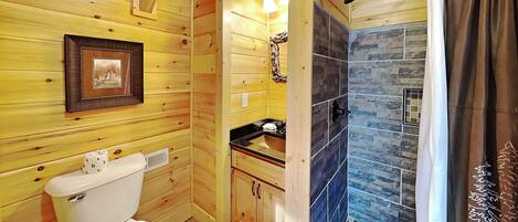 Baño de cabaña de madera con inodoro, lavamanos y zona de ducha.