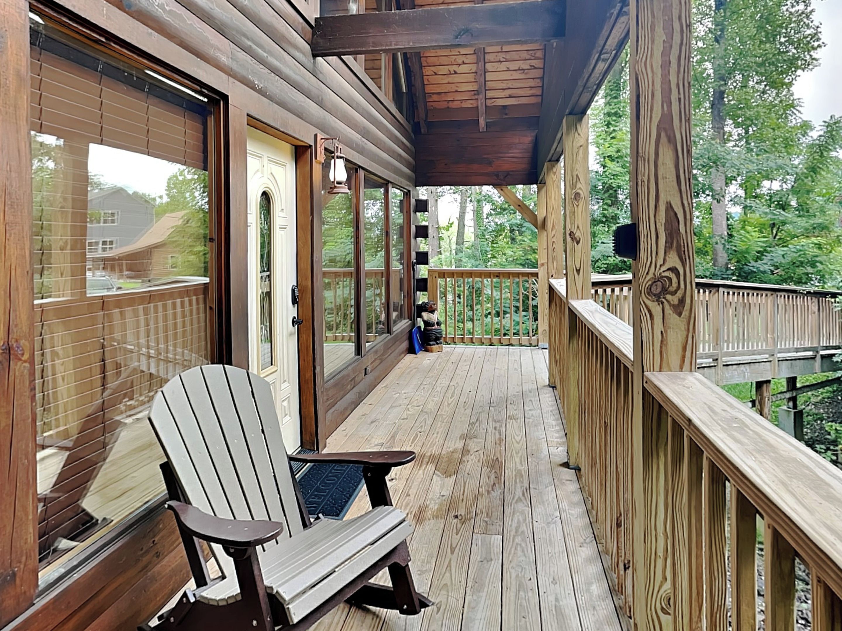 Une terrasse en bois avec un fauteuil Adirondack, des portes vitrées et une vue sur une zone boisée.