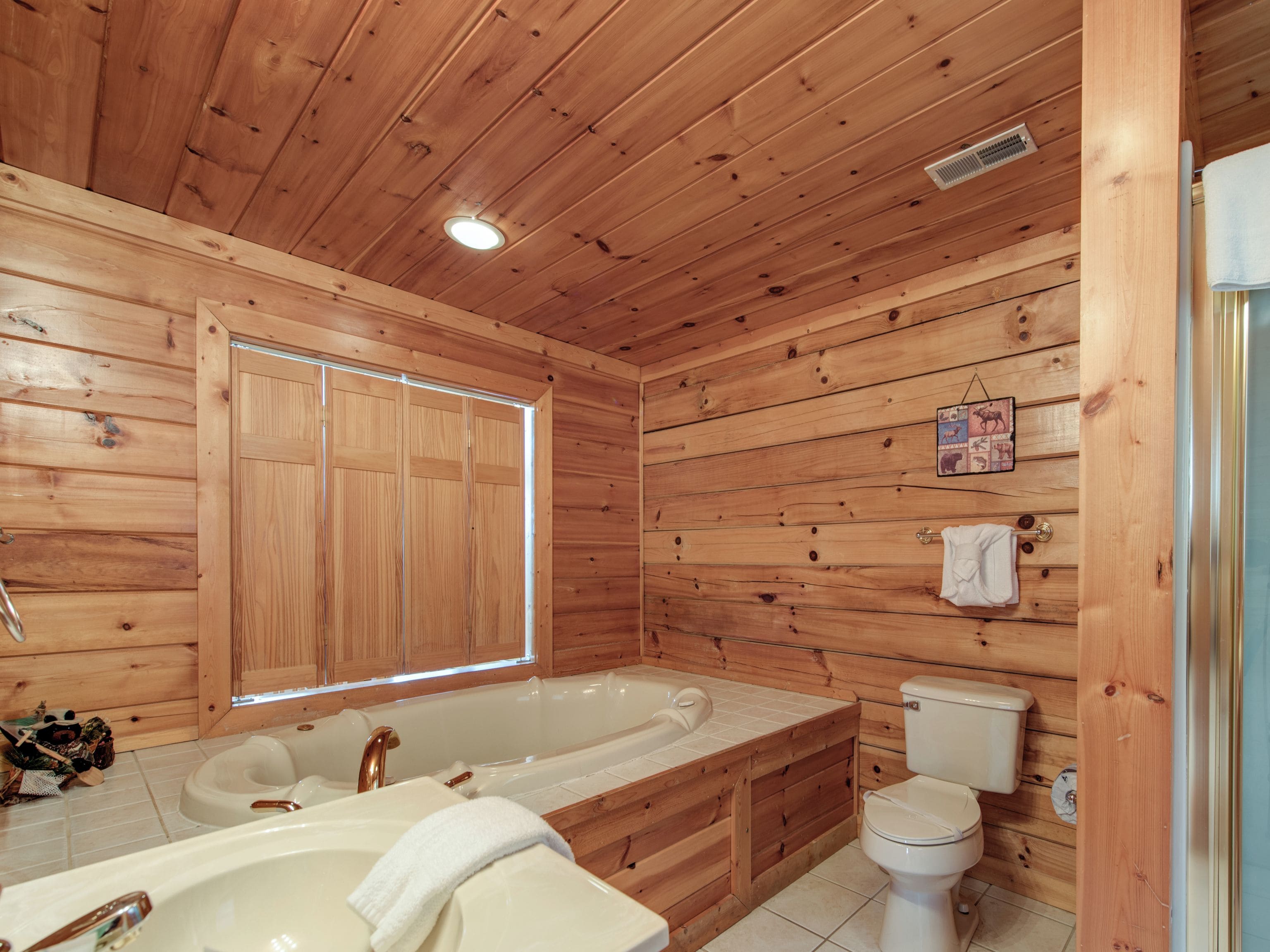 A wooden cabin bathroom with a large bathtub, toilet, and sink.