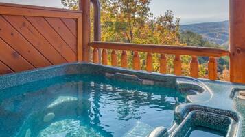 Un jacuzzi con agua cristalina, rodeado de una terraza y barandilla de madera, con vistas a un paisaje montañoso.