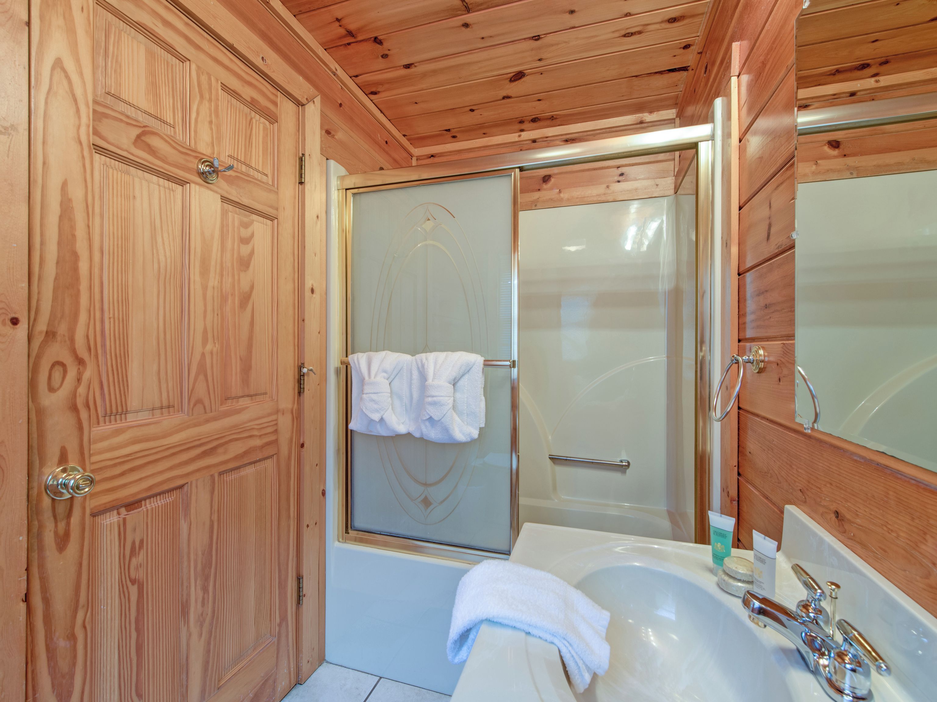 Un baño con paneles de madera, mampara de cristal, bañera y lavamanos.