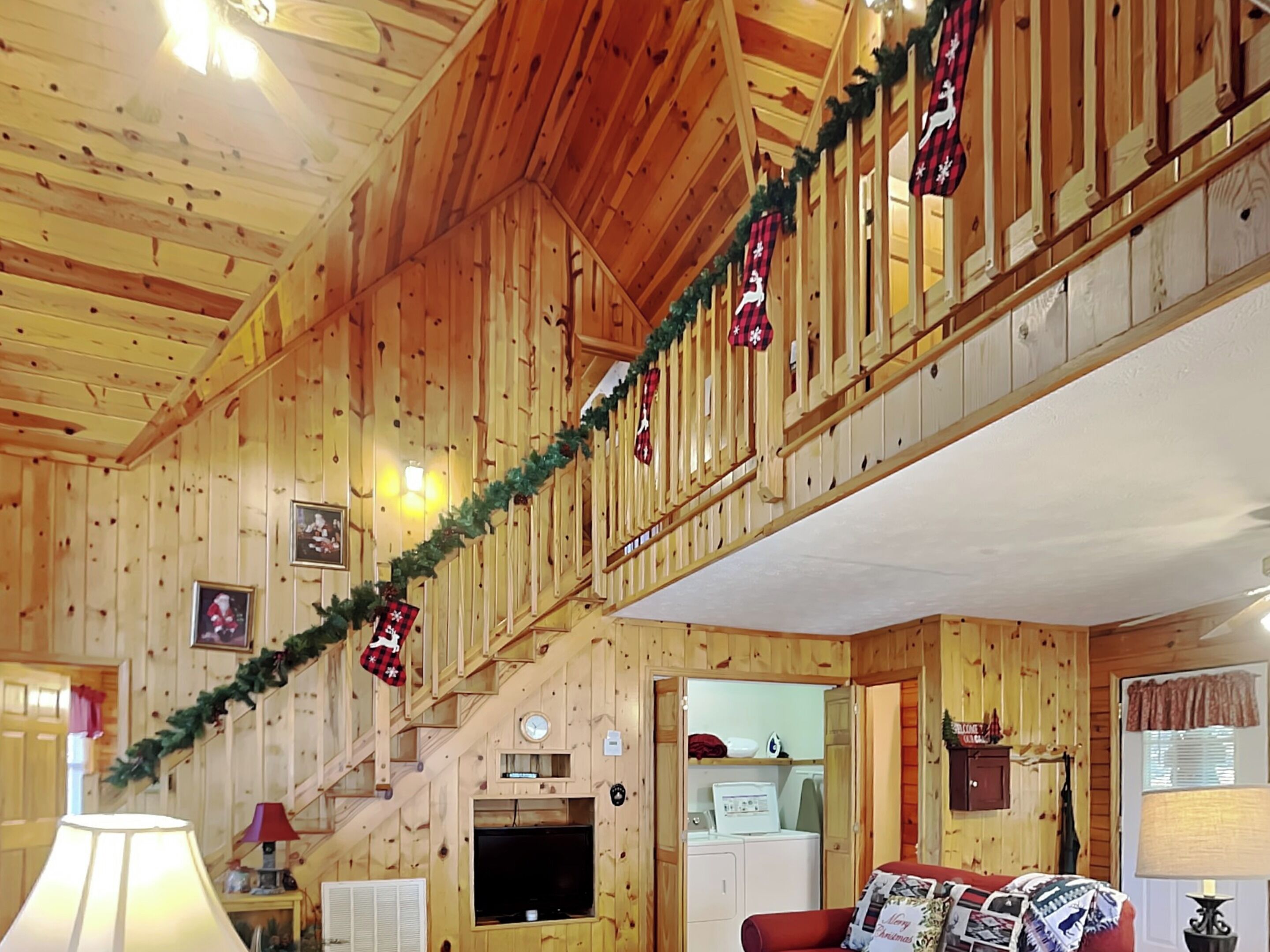 Interior d'una cabana de fusta amb escala, televisió i un sofà vermell.