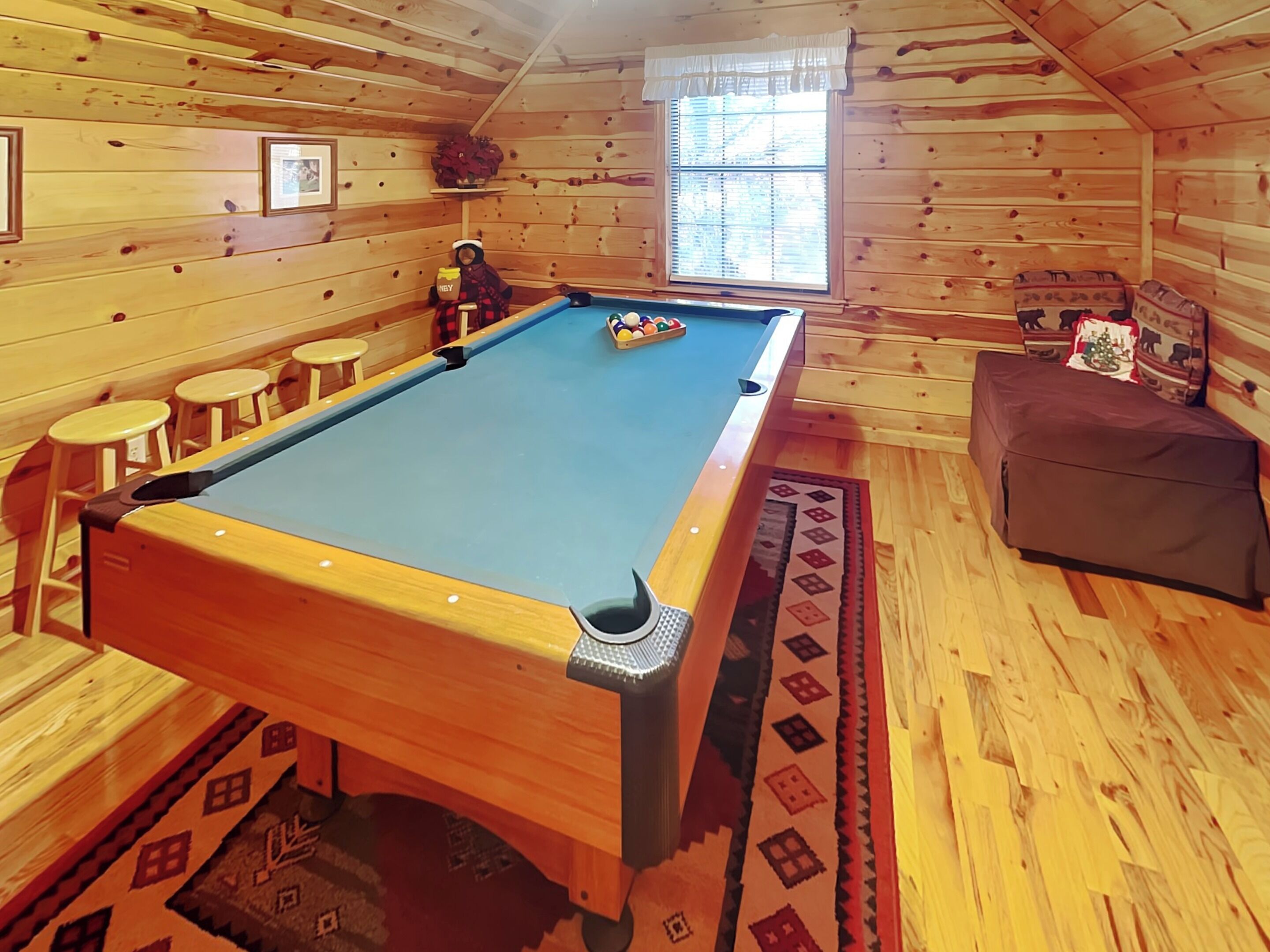 Een pooltafel in een houten kamer met een raam, krukken en een bank.
