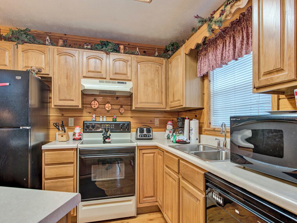 A compact kitchen with wooden cabinets, a refrigerator, stove, microwave, and a sink.
