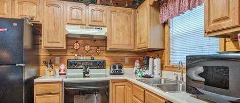 A compact kitchen with wooden cabinets, a refrigerator, stove, microwave, and a sink.