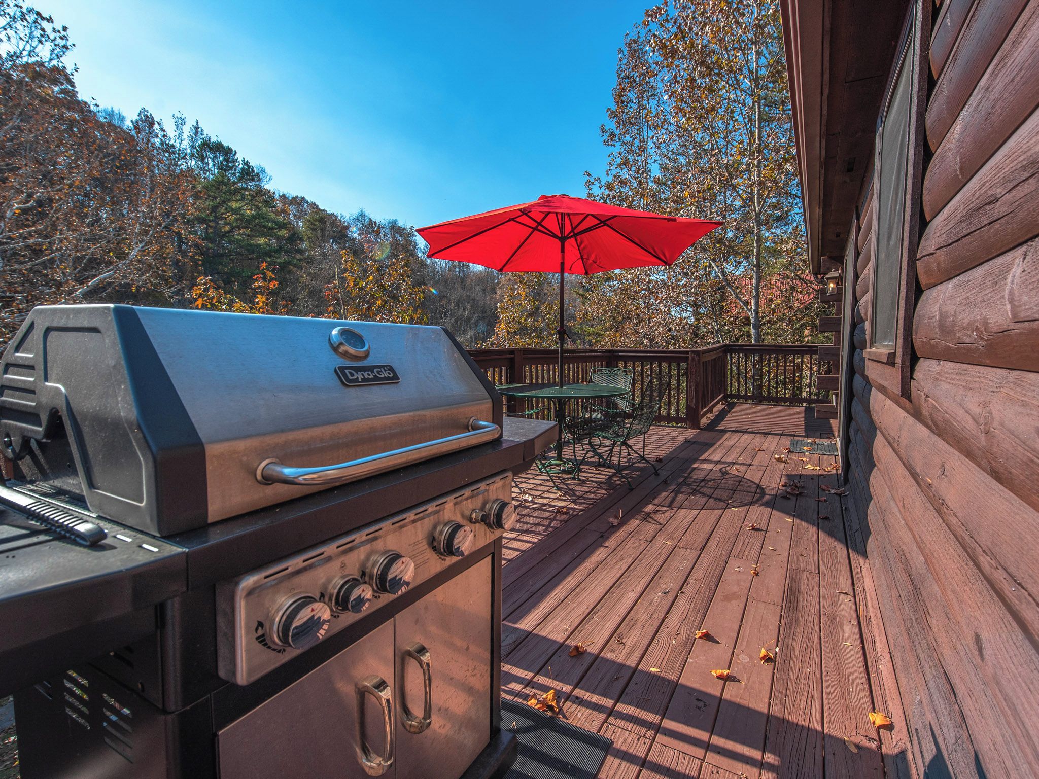 Una terraza de madera con una parrilla, una mesa y una sombrilla.