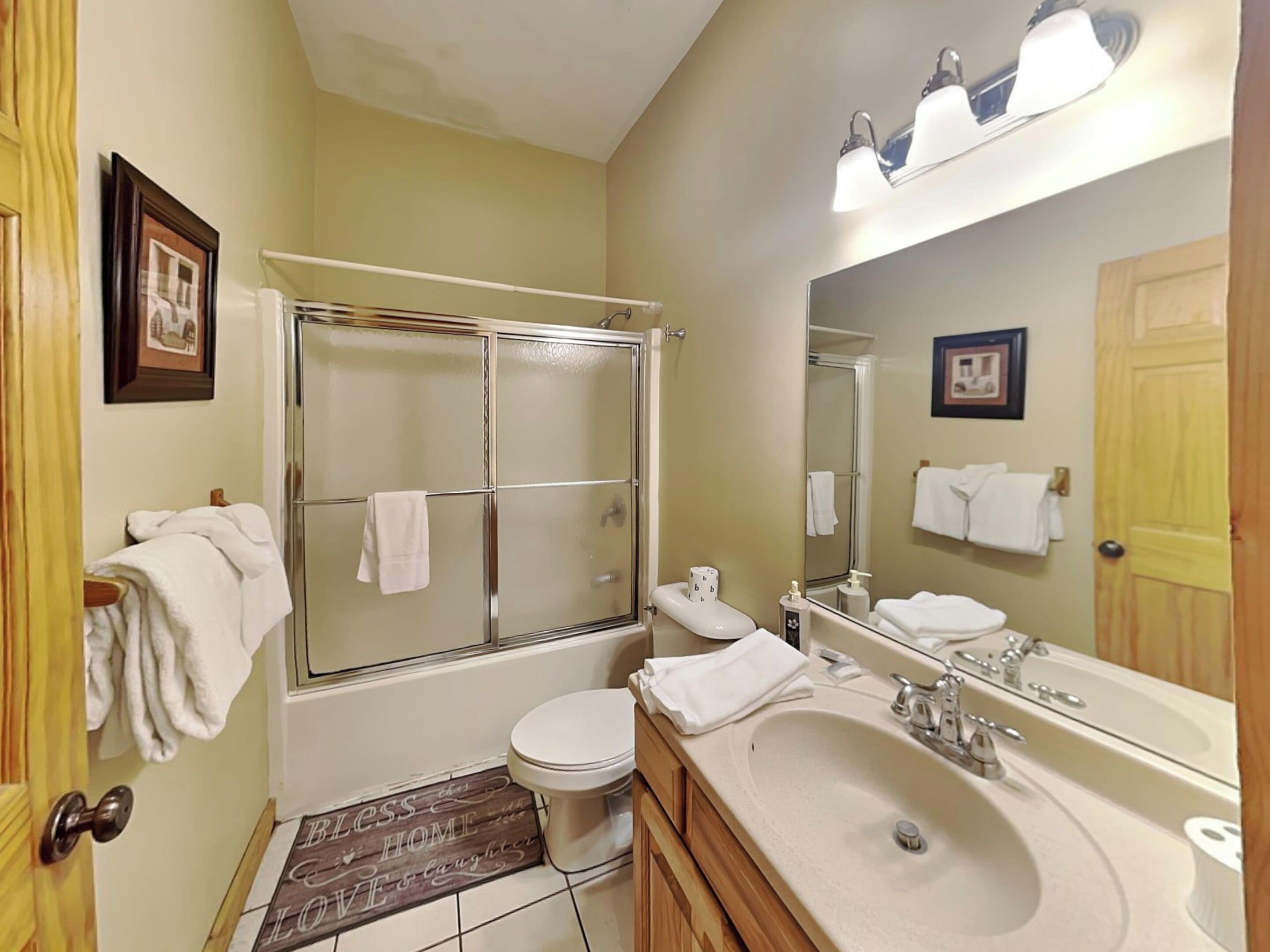 A bathroom with a bathtub, toilet, sink, and a large mirror. There are towels hanging on the wall and a shower curtain.