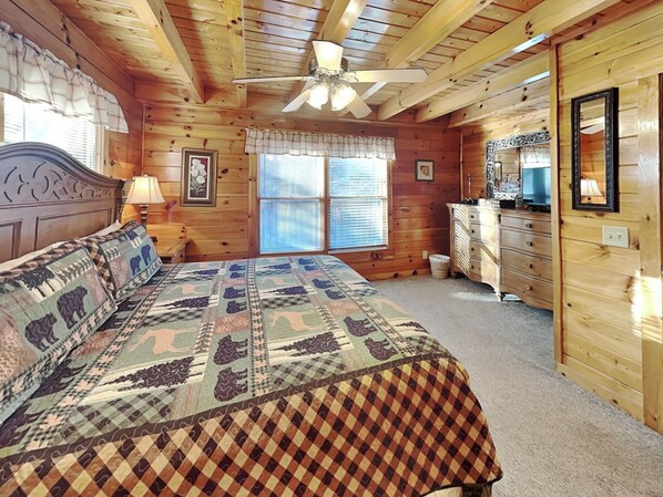 A wooden cabin bedroom with a bed, dresser, and ceiling fan.