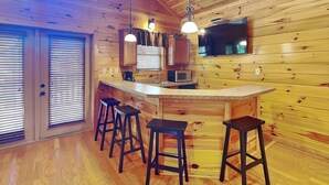 A wooden cabin interior with a kitchen area, bar stools, and a television. - Mountain View Lodge by Jackson Mountain Rentals (Gatlinburg)