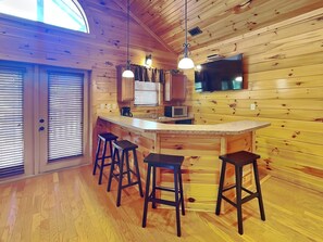 A wooden cabin interior with a kitchen area, bar stools, and a television. - Mountain View Lodge by Jackson Mountain Rentals (Gatlinburg)