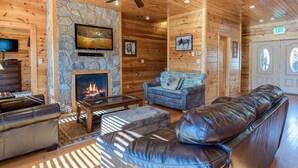 A log cabin interior with a stone fireplace, leather sofas, and a television. - Mountain View Lodge by Jackson Mountain Rentals (Gatlinburg)