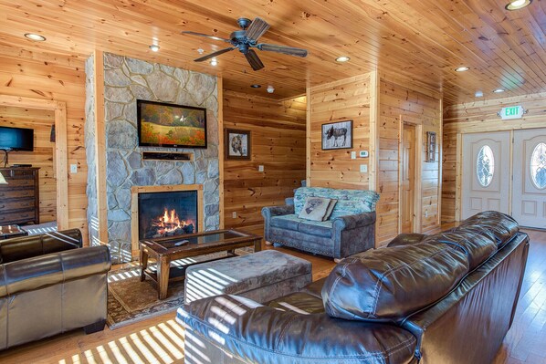 Ein Holzblockhaus-Interieur mit Kamin aus Stein, Ledersofas und einem Fernseher.