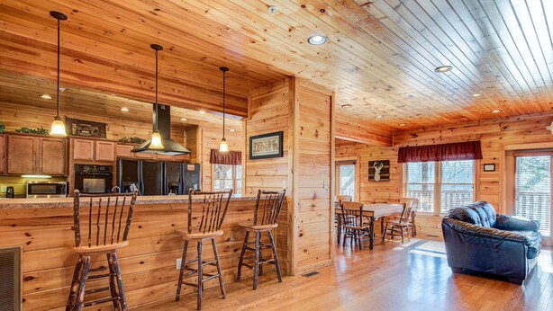 A wooden cabin interior with a bar area, dining table, and a sofa. - Mountain View Lodge by Jackson Mountain Rentals (Gatlinburg)