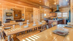 A spacious wooden dining area with a stone fireplace, wooden ceiling, and a large kitchen area with wooden cabinets and a sink. - Mountain View Lodge by Jackson Mountain Rentals (Gatlinburg)