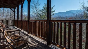 A wooden deck with chairs and tables, overlooking a mountainous landscape. - Mountain View Lodge by Jackson Mountain Rentals (Gatlinburg)